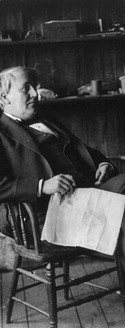 Image of Edison. Full length, seated, holding paper, facing right.